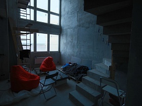 красные кресла-мешки, стул, подручный журнальный стол и лежак из деревянных поддонов в комнате с винтовой лестницей на второй этаж недостроенного пентхауса молодежи