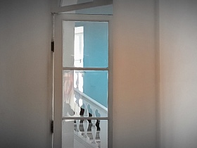 Вид сквозь стеклянную двер на белую мраморную лестницу в Усадьбе