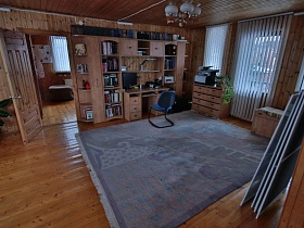 черное кресло у бежевой стенки с компьютерем, книжками на полках,большой серый ковер на полу просторного холла уютной деревянной загородной дачи