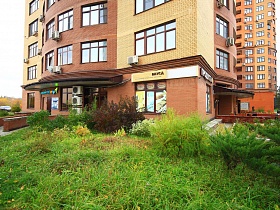 зеленые газоны перед современным многоэтажным домом с кирпичными стенами продуктового магазина на первом этаже