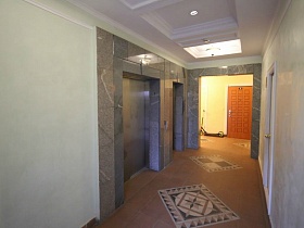 серая мраморная отделка стены лифтовых кабин на площадке этажа с коричневой плиткой на полу, белыми стенами и потолком жилого кирпичного дома