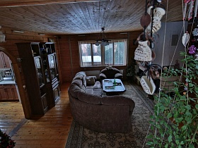 белые жалюзи на большом окне гостиной с мягкой мебелью и коричневой стенкой с посудой в уютной загородной даче