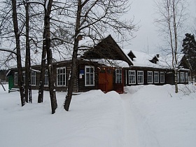 старинная деревянная школа с деревянным крыльцом под навесом на торце здания на заснеженном дворе