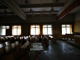 прямоугольный стол с бумагами перед рядами театральных стульев в просторном конференц зале для военных с желтыми стенами и желтыми шторами на больших окнах