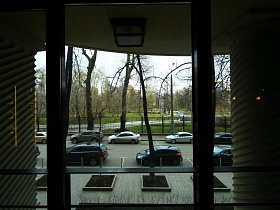 легковые машины на парковочных местах вдоль металлического забора вокруг зеленого парка и напротив окон ресторана лофт