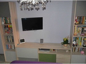 бежевая стенка с книгами и телевизором на стене напротив деревянной кровати в детской спальне