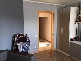 одежда на напольной деревянной вешалке у серой стены и светлый шкаф для одежды у открытой двери в детскую спальную комнату современной трехкомнатной квартиры