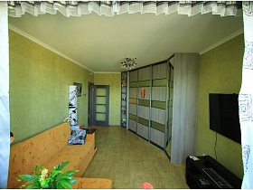 серо зеленый угловой шкаф в гостиной с зелеными стенами двухкомнатной квартиры новостроя