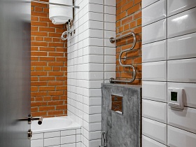 водонагревательный бак на стене с белым кафелем, над белой ванной зашитой белой плиткой у кирпичной стены в ванной комнаты