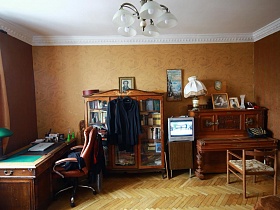 белые плафоны люстры на белом потолке с лепниной в спальной комнате с длинным рабочим столом, пианино и книжным шкафом в советской трехкомнатной квартире