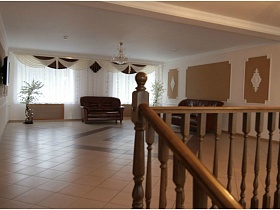 два коричневых мягких дивана в красивом просторном холле на втором этаже с оригинальными шторами на окнах