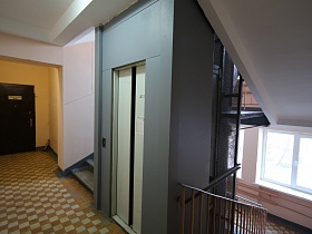 белый потолок и розовые стены ухоженного подъезда с шахматной плиткой на полу, с лифтом и лестничными маршами между этажами
