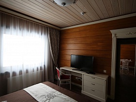 плоский телевизор на белом длинном столе с ящиками у стены спальни в современном деревянном коттедже