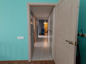 открытая дверь из спальни в голубую прихожую с белыми шкафами у стены и светлым полом квартиры в сталинском доме с элементами лофт