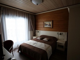 большая кровать с бежево коричневым покрывалом и бежевыми подушками в спальне деревянного съемного коттеджа