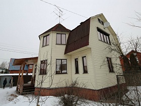 интересной и необычной постройки загородный двухэтажный домик с высоким цоколем на дачном участке зимой