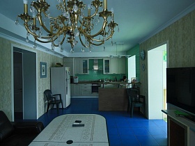 общий вид просторной светлой кухни с белой мебельной стенкой, столом и диваном на синем полу