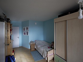 голубой коврик, плетенная корзина у деревянной кровати с бежевым покрывалом, шкаф для одежды у голубой стены с картинами детской комнаты стильной трешки в Икеа стиле