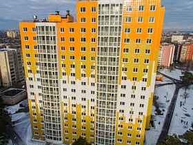 современное многоэтажное желтое с белыми вставками  жилое разновысотное здание новостройки с застекленными лоджиями