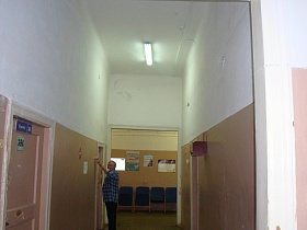 лампы дневного света на белом потолке светлого коридора с розовыми панелями на высоких стенах,открытым дверным проемом в длинный коридор с палатами для больных