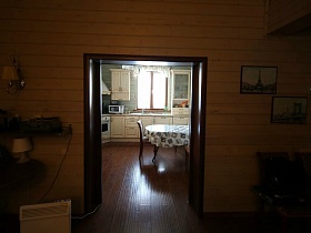 открытая дверь на кухню с белой мебелью и круглым столом современного деревянного дома