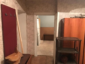 вишневая настенная вешалка с крючками и деревянный брусок у входной двери в прихожей с темной этажеркой и шкафом для одежды