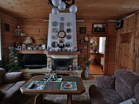 настольная лампа, фотографии на полочке, телевизор на столике у камина с плиткой под кирпич в гостиной загородной дачи