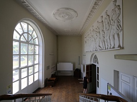 просторное фойе первого этажа с большим арочным окном, лепниной на белом потолке и лепными фигурами большой картины над входной дверью