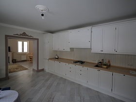 плинтуса цвета капучино переходят в отделку дверного проема светлой кухни с белой мебельной стенкой