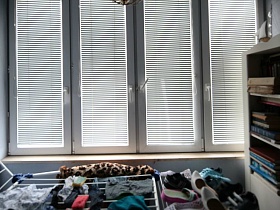 сушилка с бельем и обувью, белый шкаф с книгами в застекленной лоджии с жалюзями на окнах простой семейной квартире