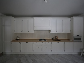 белая кухня с множеством шкафчиков, ящичков на всю стену со светлой коричневой столешницей