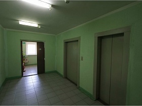 просторный холл у дверей лифта с салатневыми стенами и длинными светильниками на потолке