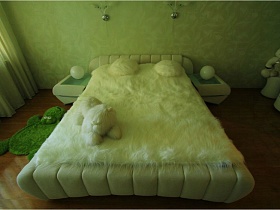 белая кровать с белым меховымым покрывалом и пушистыми подушками в спальне простой двушки