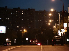 современные многоэтажные дома в жилом квартале города вдоль улицы Крылатские Холмы с подсвеченными дорожными знаками вдоль дороги под ярким освещением фонарных столбов