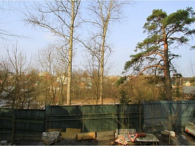 разнообразный строительный материал вдоль высокого зеленого забора вокруг дома в сосновом лесу
