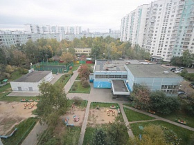 баскетбольная площадка за высоким зеленым забором у детского садика с игровыми детскими участками в квартале с высотными жилыми домами