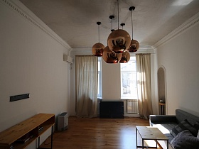 шесть сферических больших кремовых светильника на белом потолке гостиной с деревянными письменным столиком у стены в зонированной комнате современной скандинавской квартиры