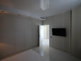 плоский телевизор на светлой стене черно белой спальной комнаты с открытой дверью