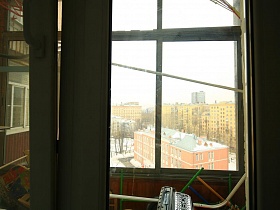 застекленный захламленный балкон через стекло балконной двери в семейной трехкомнатной квартире эпохи СССР