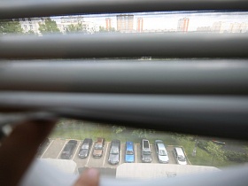 вид сквозь жалюзи на окне на припаркованные машины во дворе многоэтажного дома в новострое