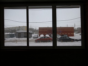 строительный вагончик, машины в снегу, кирпичное одноэтажное здание напротив жилого дома с просторной современной квартирой на первом этаже жилого многоэтажного кирпичного дома
