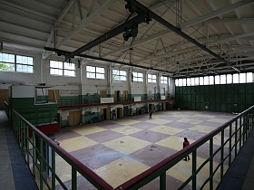 огромное помещение лофт здания с шахматным полом и зелеными металлическими перилами на втором этаже