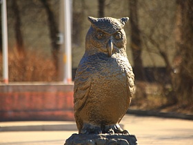 статуя строгой совы - символа мудрости на постаменте на круглой клумбе на въезде в городок Сычево для съемок кино