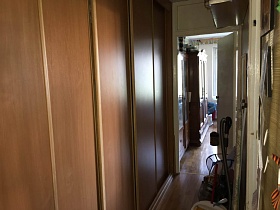 длинный пятидверный коричневый шкаф-купе в прихожей с белыми стенами и коричневым линолеумом на полу трехкомнатной квартиры