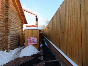 черные резиновые коврики вдоль высокого деревянного забора вокруг домов из сруба банного комплекса