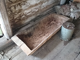 круглая канистра, большая ванночка с остатками глины у деревянной стены хозяйственной постройки дома в заброшенной деревне