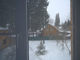 участок под снегом и соседний дом с елями сквозь окно спальни на втором этаже кирпичного добротного дома