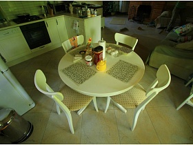 белые стулья со спинками вокруг круглого белого стола с квадратными  салфетками на светлой кухне дачи работника кино