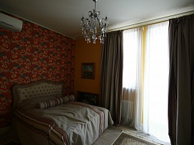 темные шторы и белая гардина на большом окне с выходом на балкон, большая двухцветная кровать с длинным полосатым валиком на светлом покрывале в спальной комнате девчачьей современной квартире