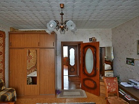 коричневый шкаф с зеркалом по центру, трельяж у стены и иконы за открытой дверью в комнаты бабушки с ковром 19005-2005 гг яркой современной трехкомнатной квартиры